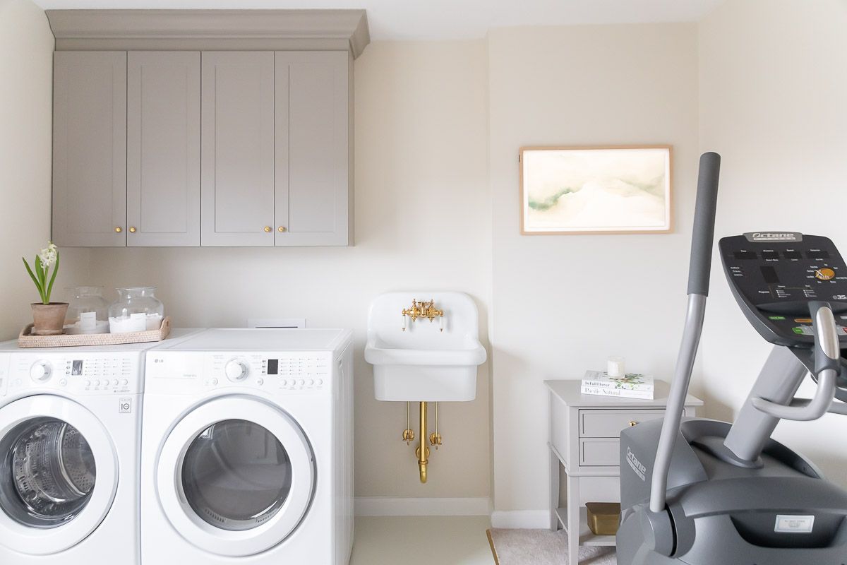 A modern laundry room with greige cabinets, a Frame TV, and an elliptical training machine.