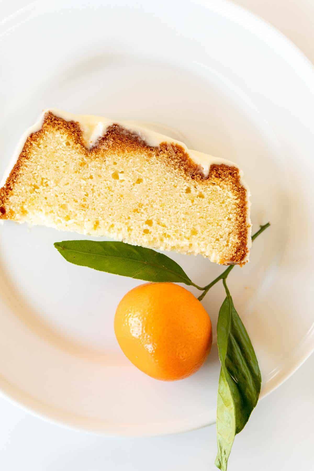 A single slice of orange pound cake on a white plate, single orange to the side.