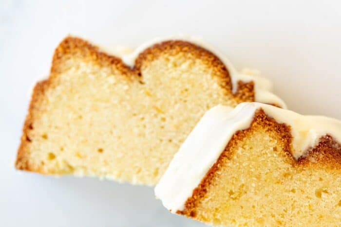 Two slices of orange pound cake topped with frosting on a white surface.