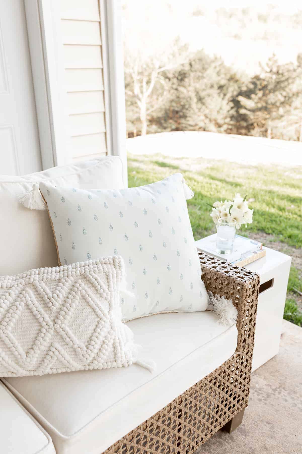 An outdoor room patio scene with a white sectional and flowers on a side table.