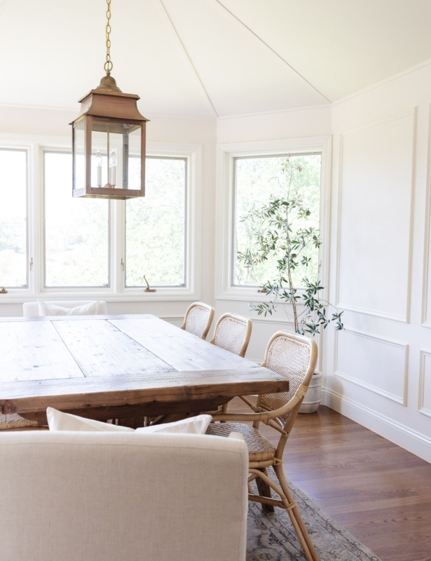 A dining room with a wood table, and walls and trim painted the same color white.