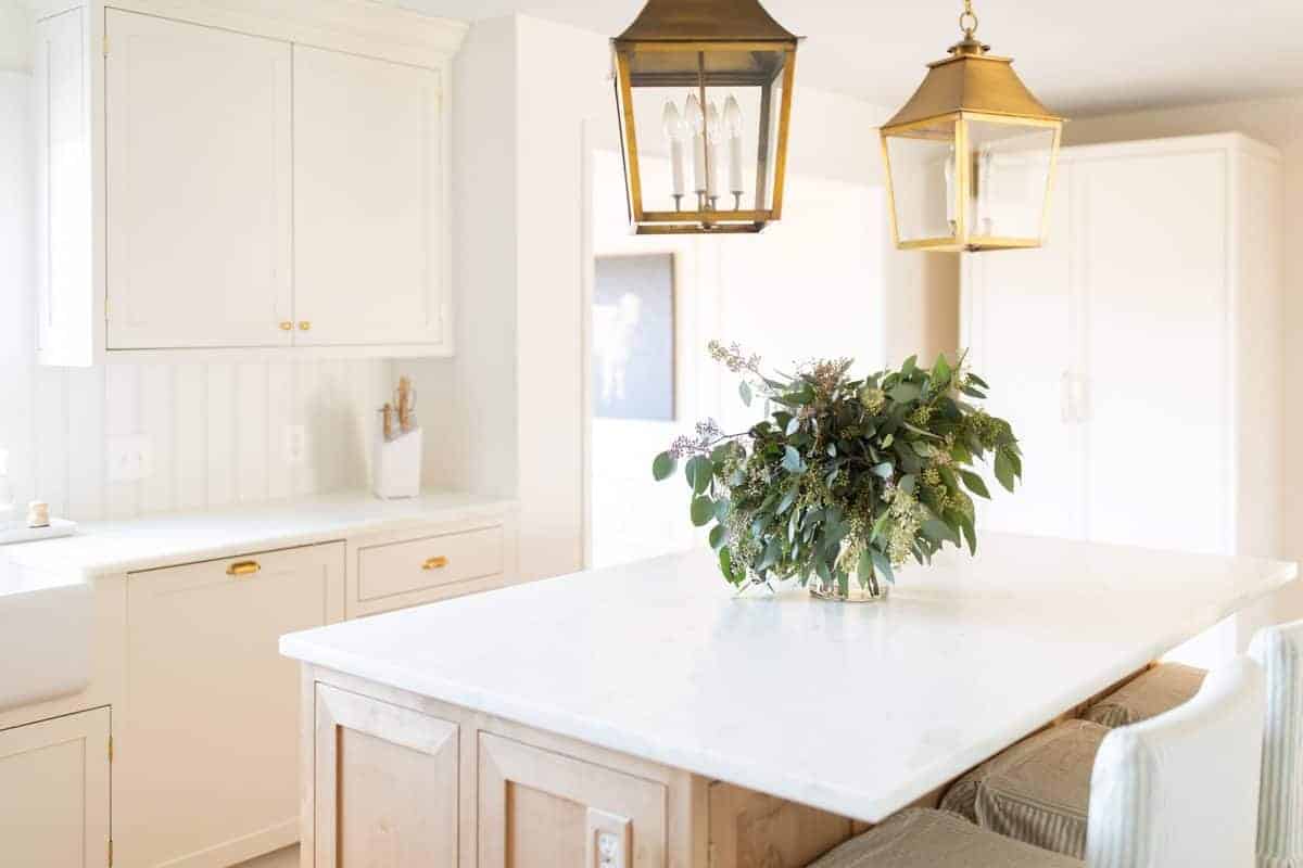 A cream kitchen with a vase of seeded eucalyptus on the island.