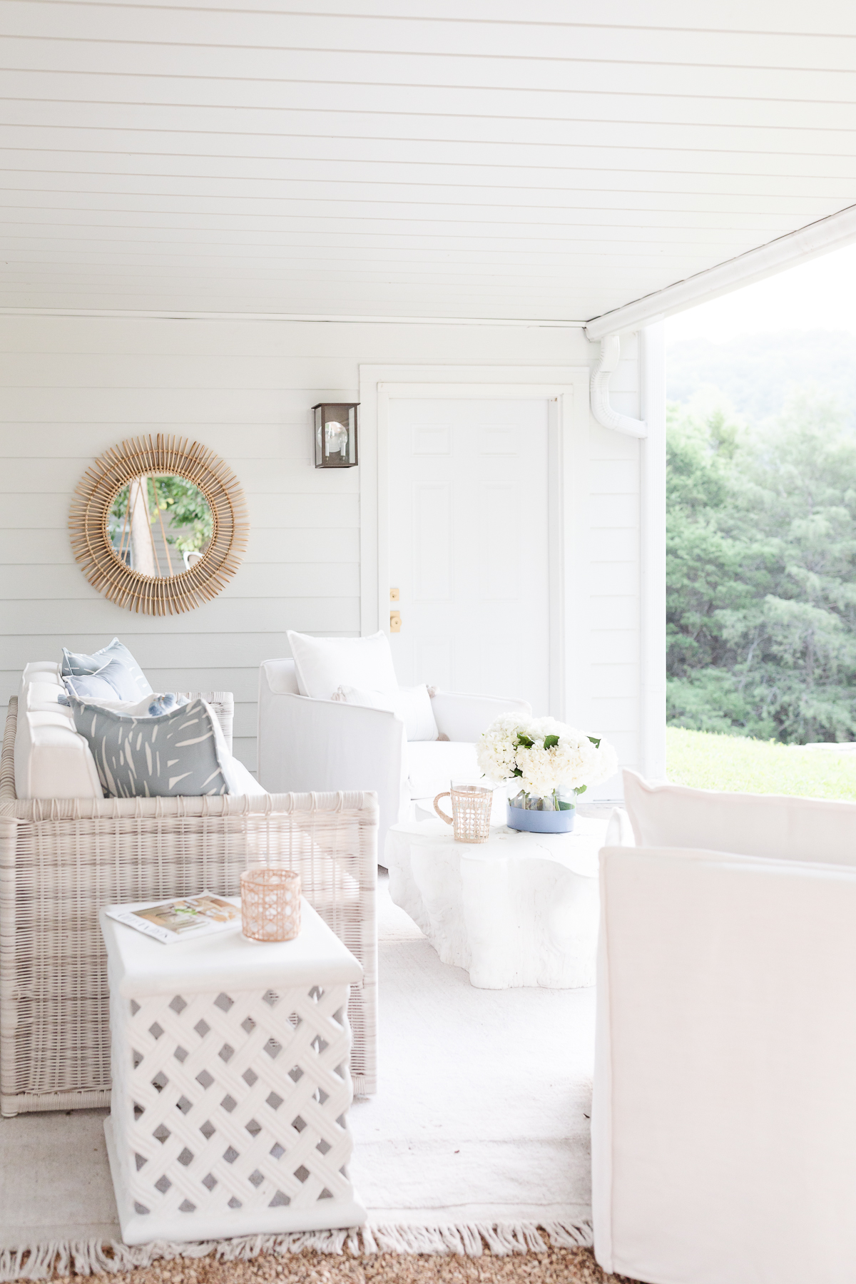 A white porch with wicker furniture and a mirror enhanced by an under deck ceiling.