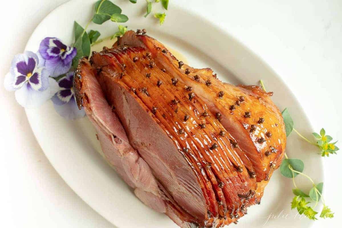 A honey ham on a white platter accented with fresh flowers