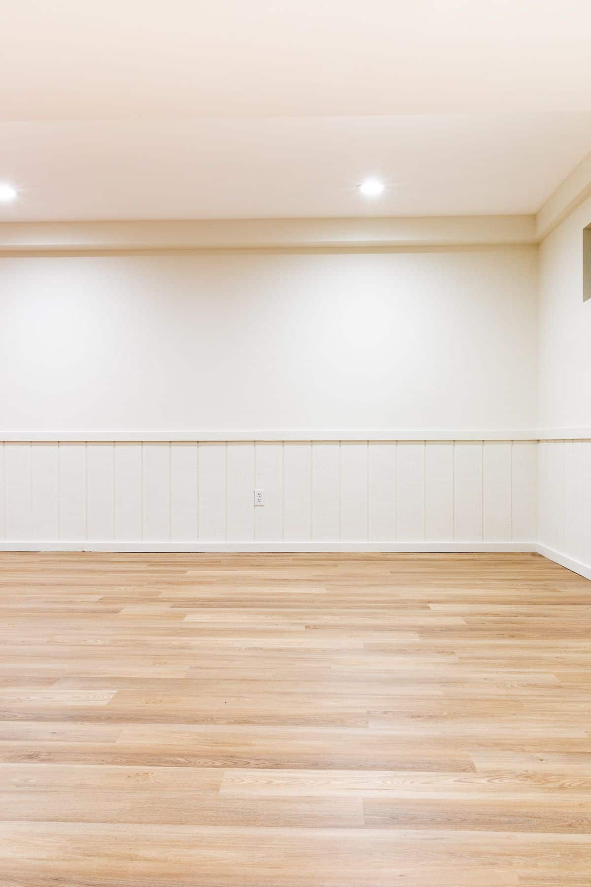 An empty basement with white walls and a medium toned vinyl plank flooring.