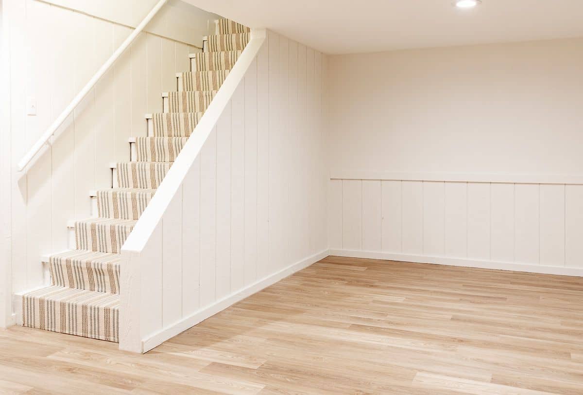 An empty basement with white walls and a medium toned vinyl plank flooring.