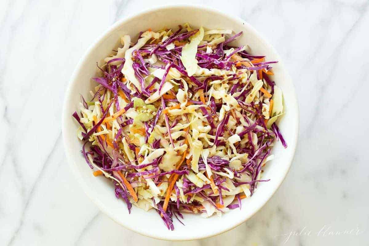 A white bowl full of cabbage salad coleslaw on a marble surface