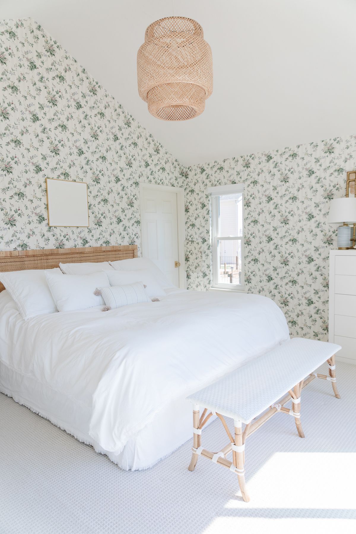 A coastal modern bedroom with floral wallpaper and a rattan headboard and light