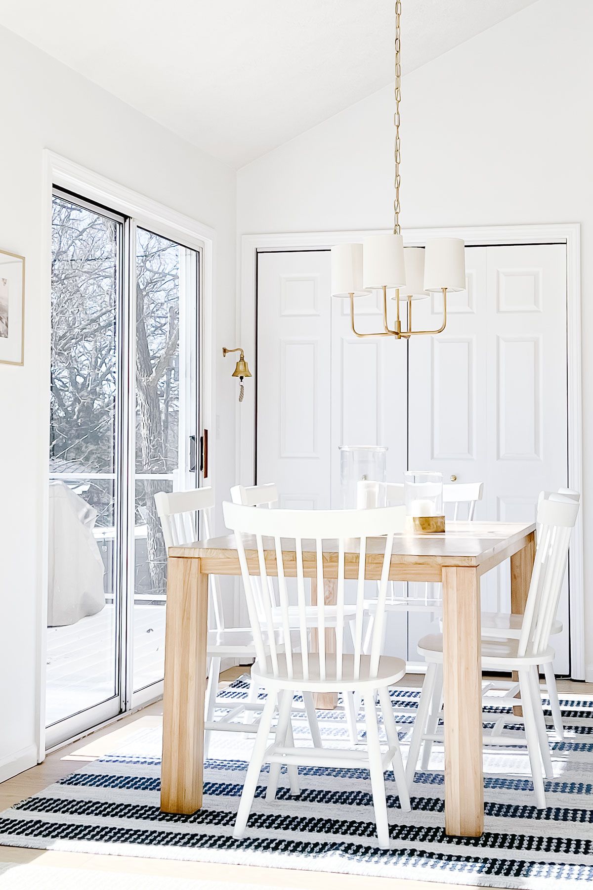 A coastal modern kitchen with a light wood table, white chairs and a blue and white striped rug