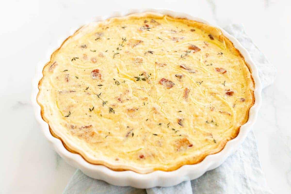 A homemade quiche in a white pie pan on a marble surface