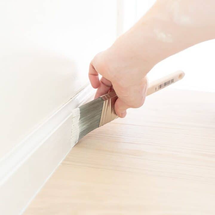 A hand painting white trim next to a light wood floor.
