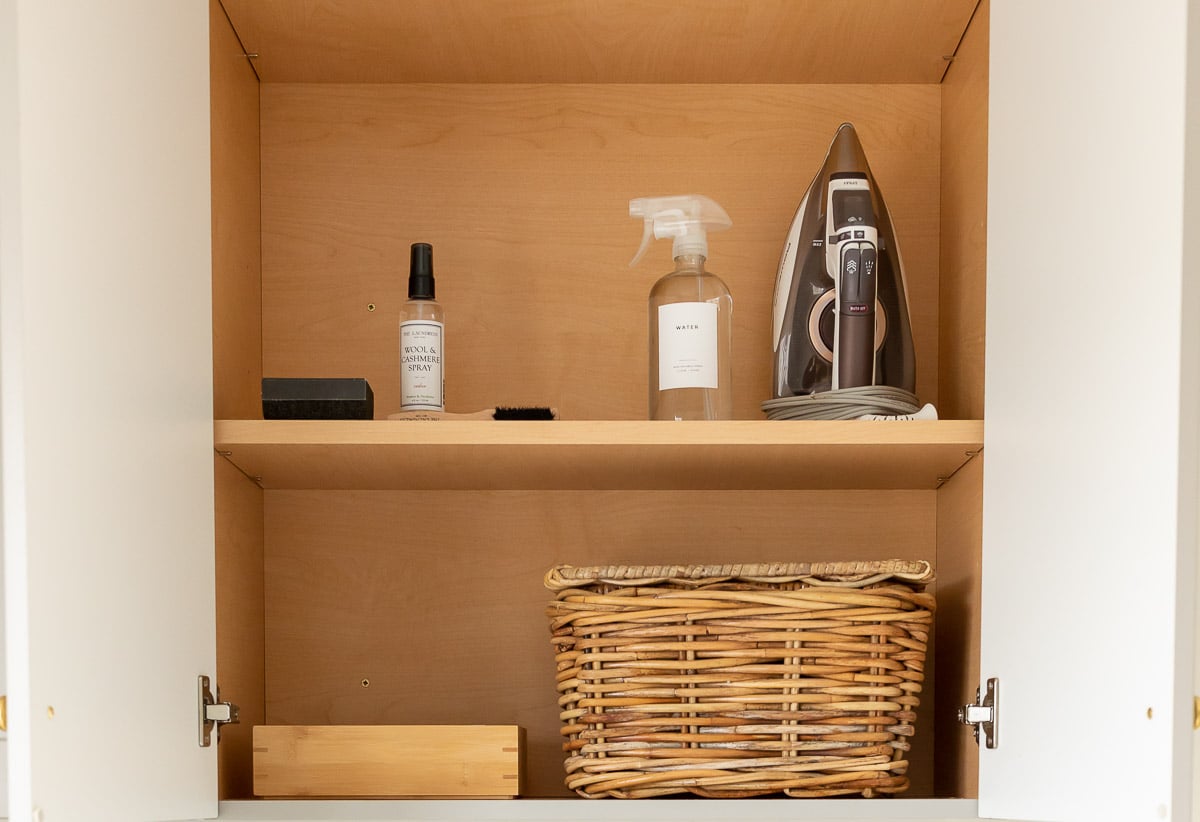 A laundry room organization cabinet featuring a wicker basket and cleaning supplies.
