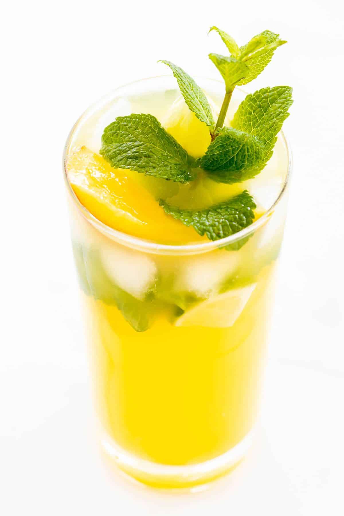 A mango mojito in a clear glass, garnished with a sprig of mint.