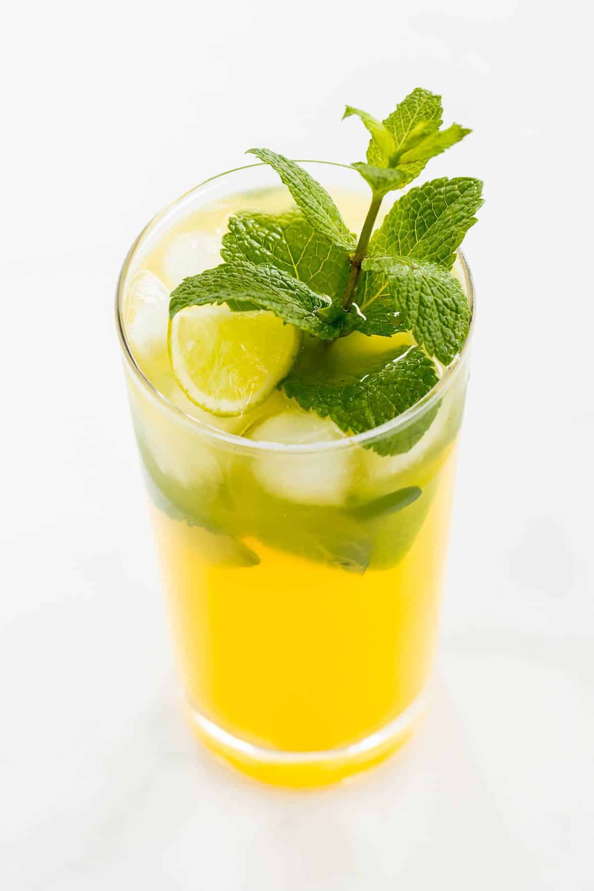 A mango mojito in a clear glass, garnished with a sprig of mint.
