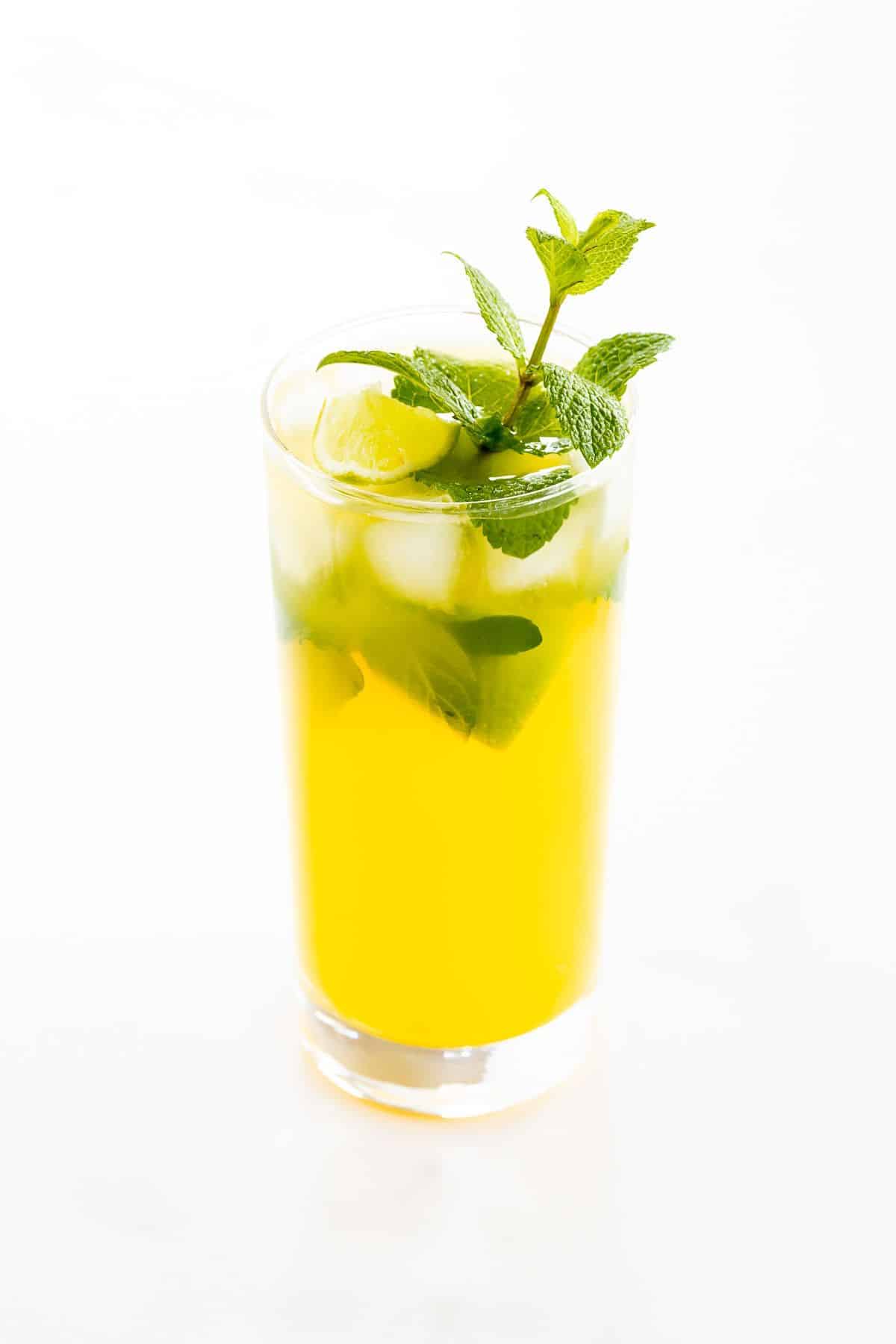A mango mojito in a clear glass, garnished with a sprig of mint.