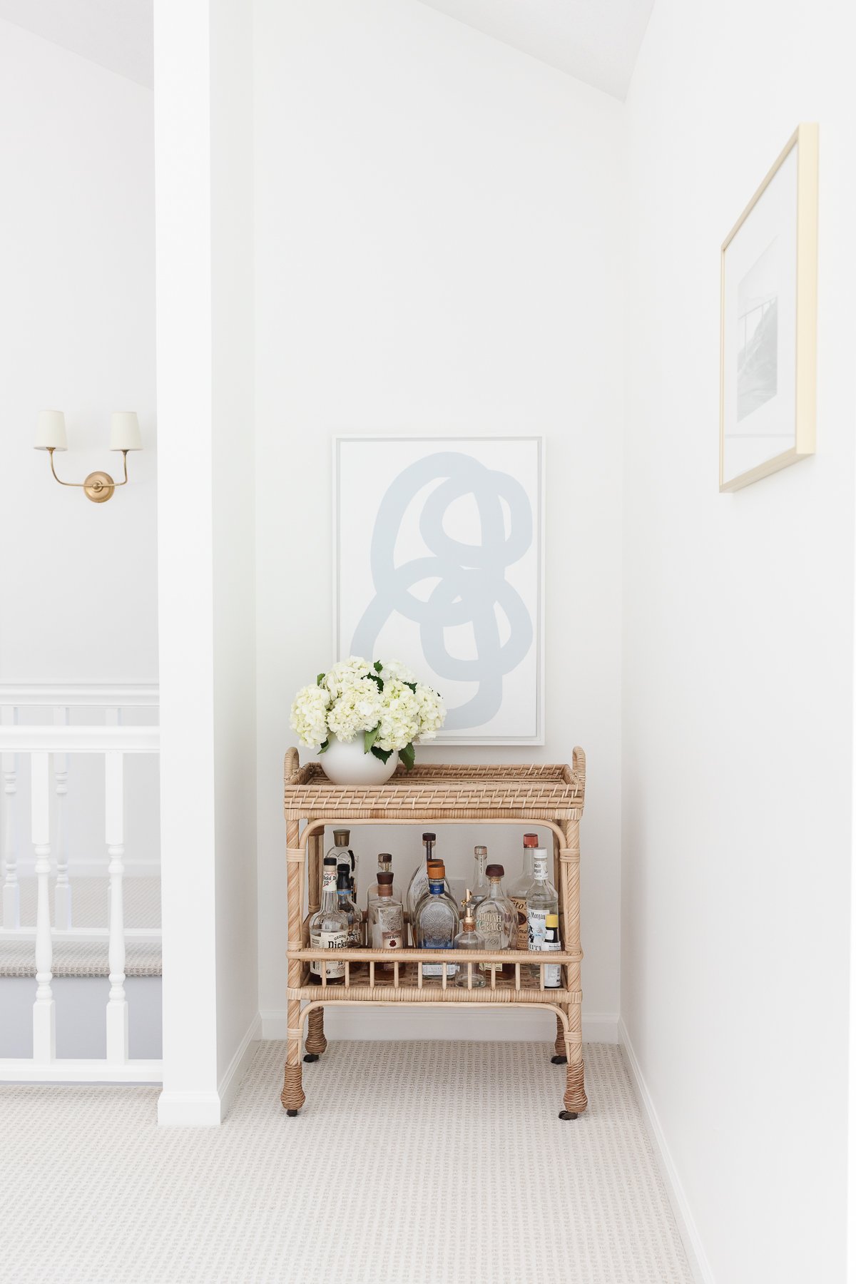 A rattan bar cart with fresh flowers, bottles of alcohol and modern blue and white art in the background.