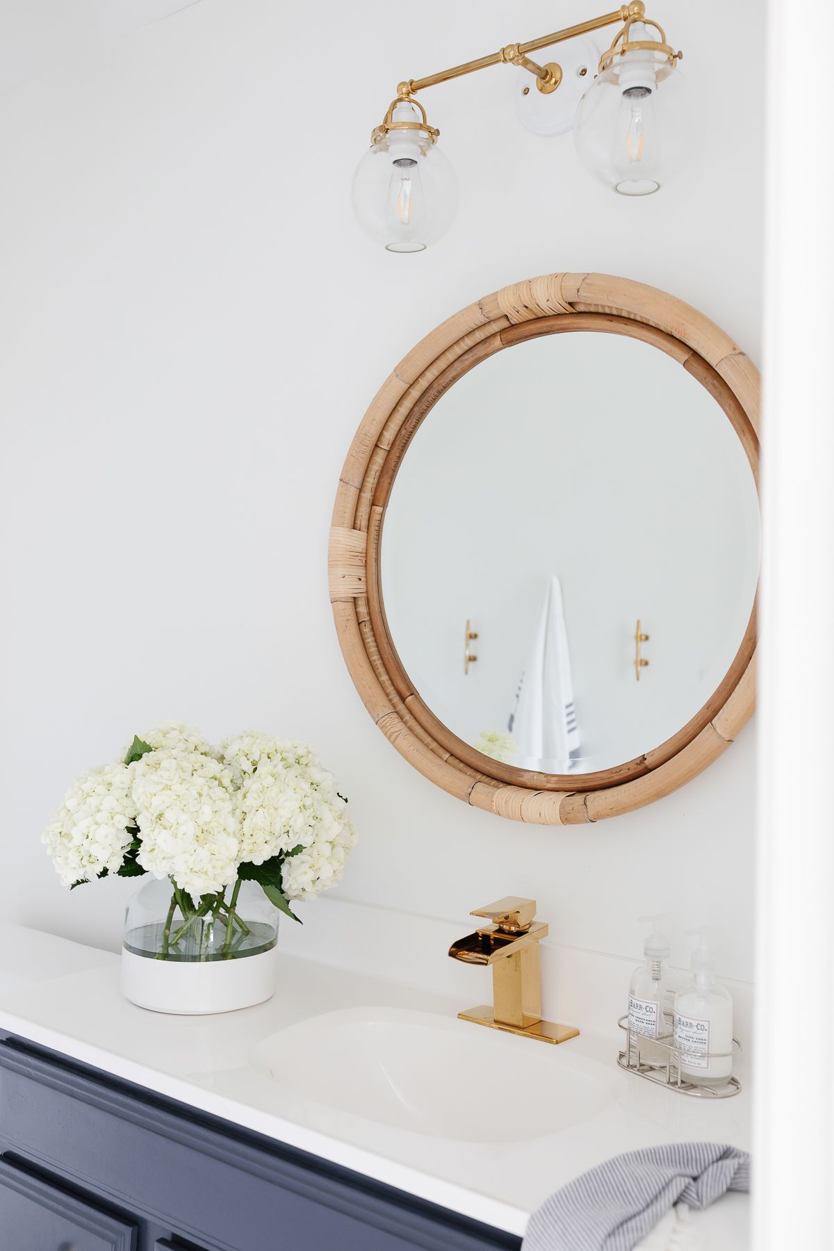 A modern coastal bath with a rattan mirror and a navy vanity