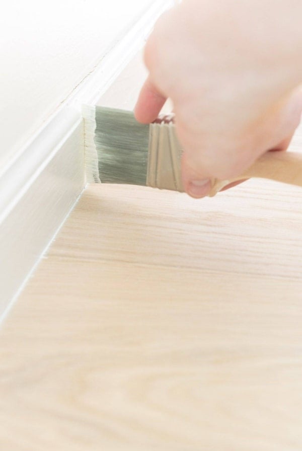 A hand painting white trim next to a light wood floor.