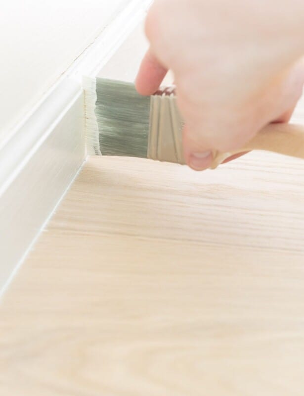 A hand painting white trim next to a light wood floor.