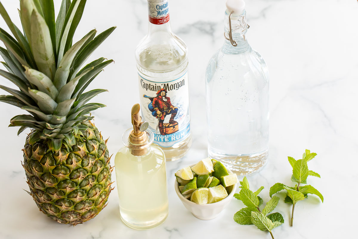 Ingredients for a pineapple mojito recipe on a marble countertop.