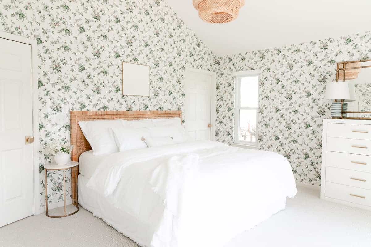 A bedroom with wallpaper and white bedding and white art over bed