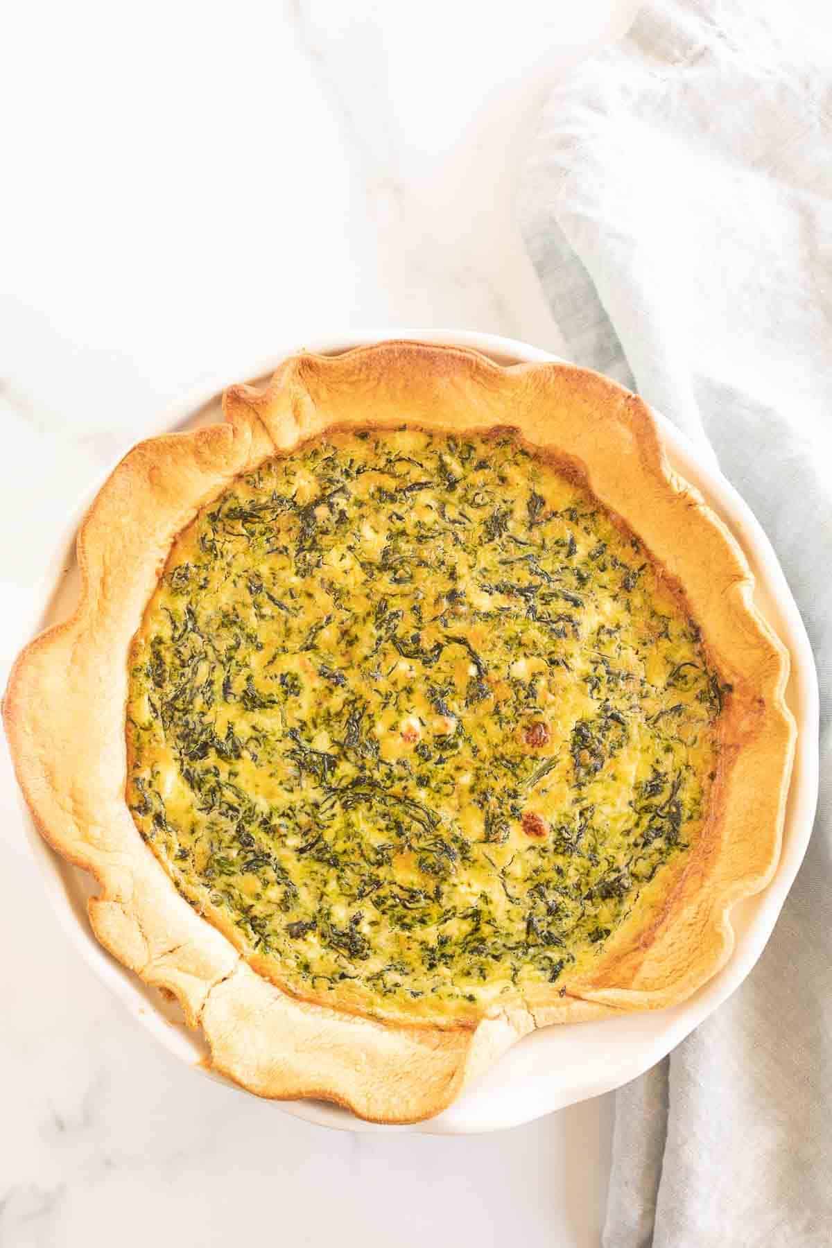 A small baked spinach quiche on a marble surface.