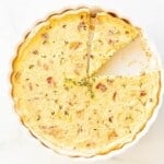 A whole quiche with two slices missing, on a white surface.