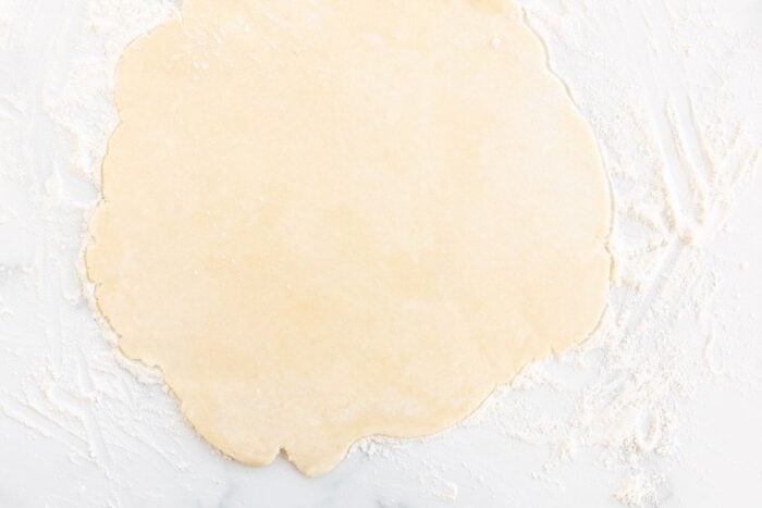 A pie crust rolled out on a marble surface.