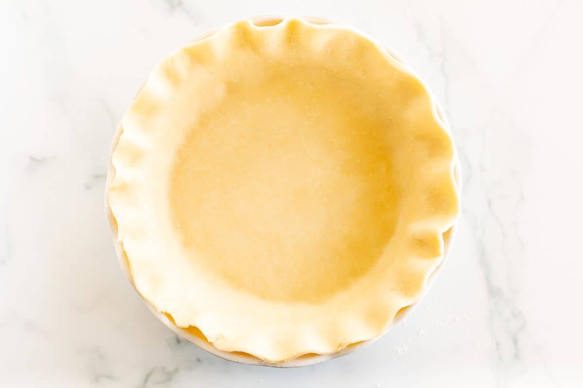 An unbaked pie crust in a white pie dish on a marble surface.