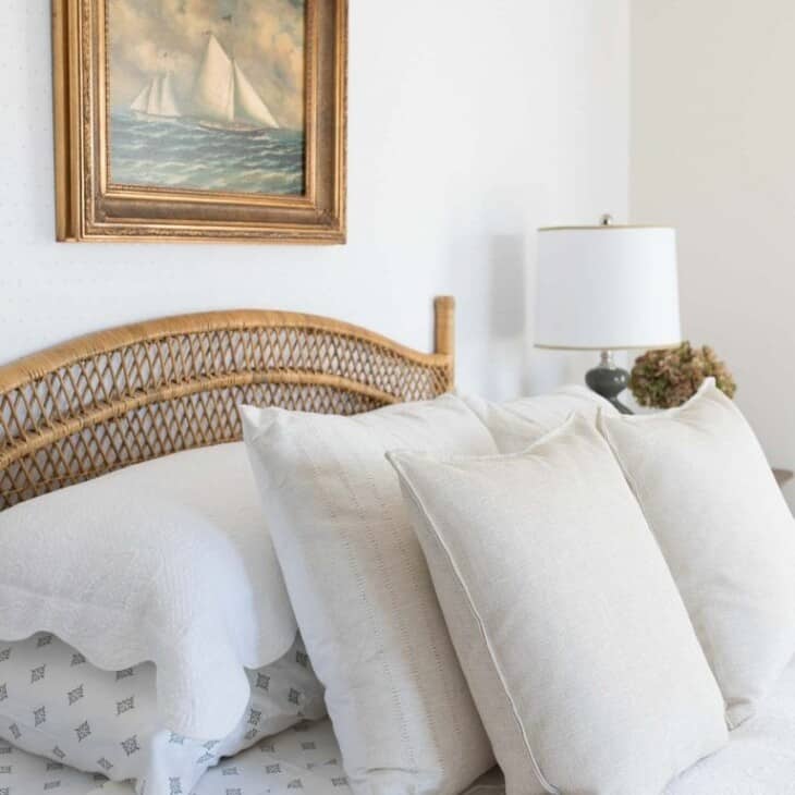 A bedroom with neutral bedding, a rattan bed, and sailboat art above headboard.