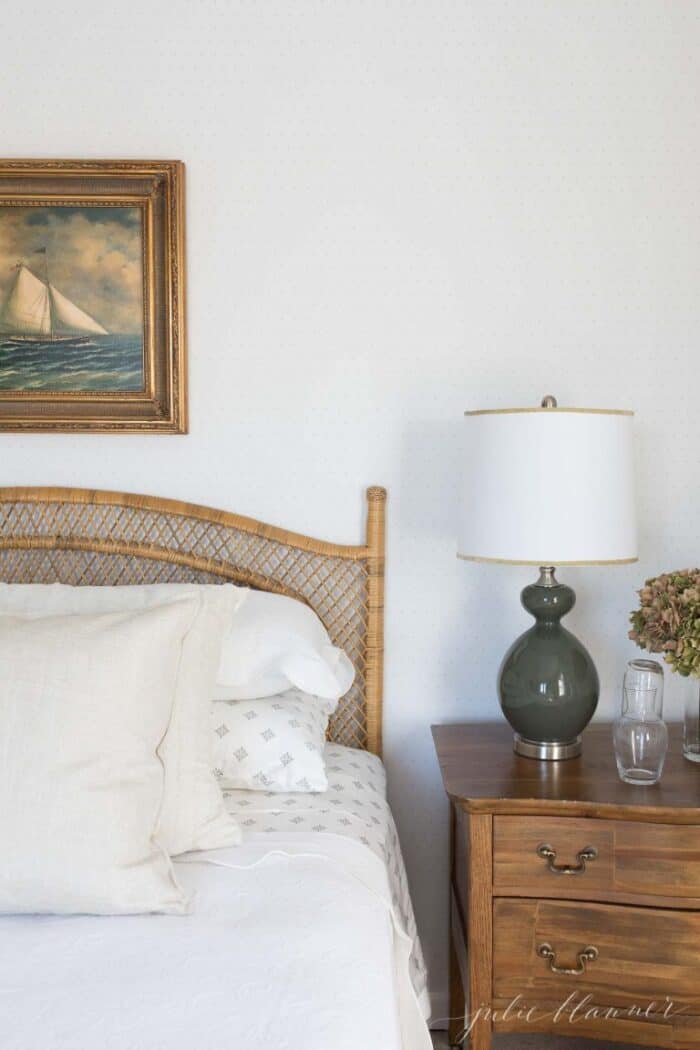 A bedroom with neutral bedding, a rattan bed, and sailboat art above headboard.