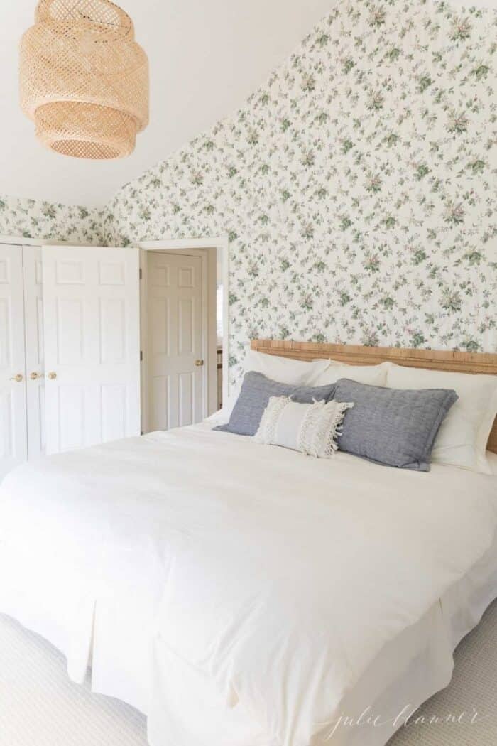A floral wallpapered bedroom with a rattan bed and white bedding.