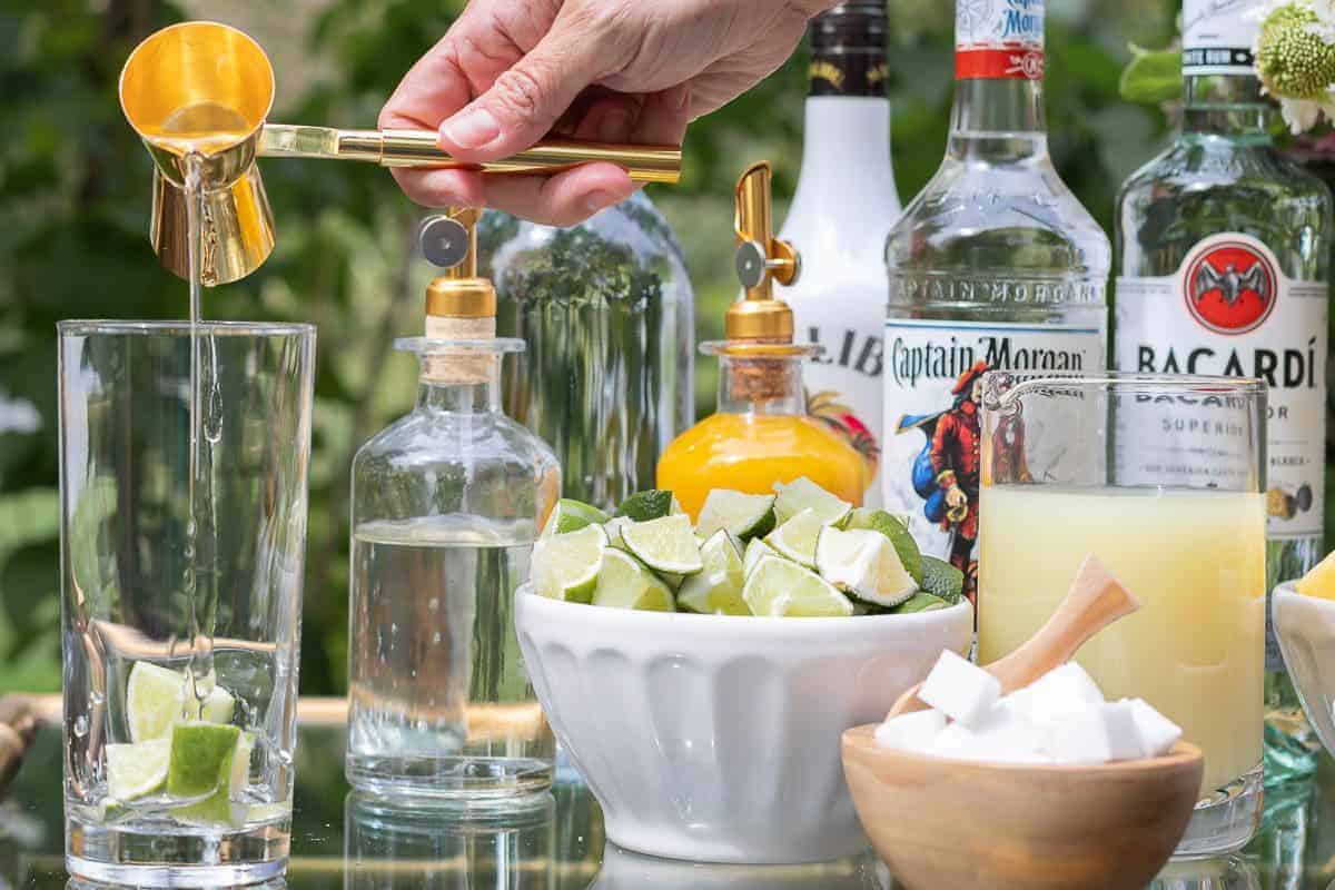 A hand reaching across a mojito bar to pour rum in a glass.