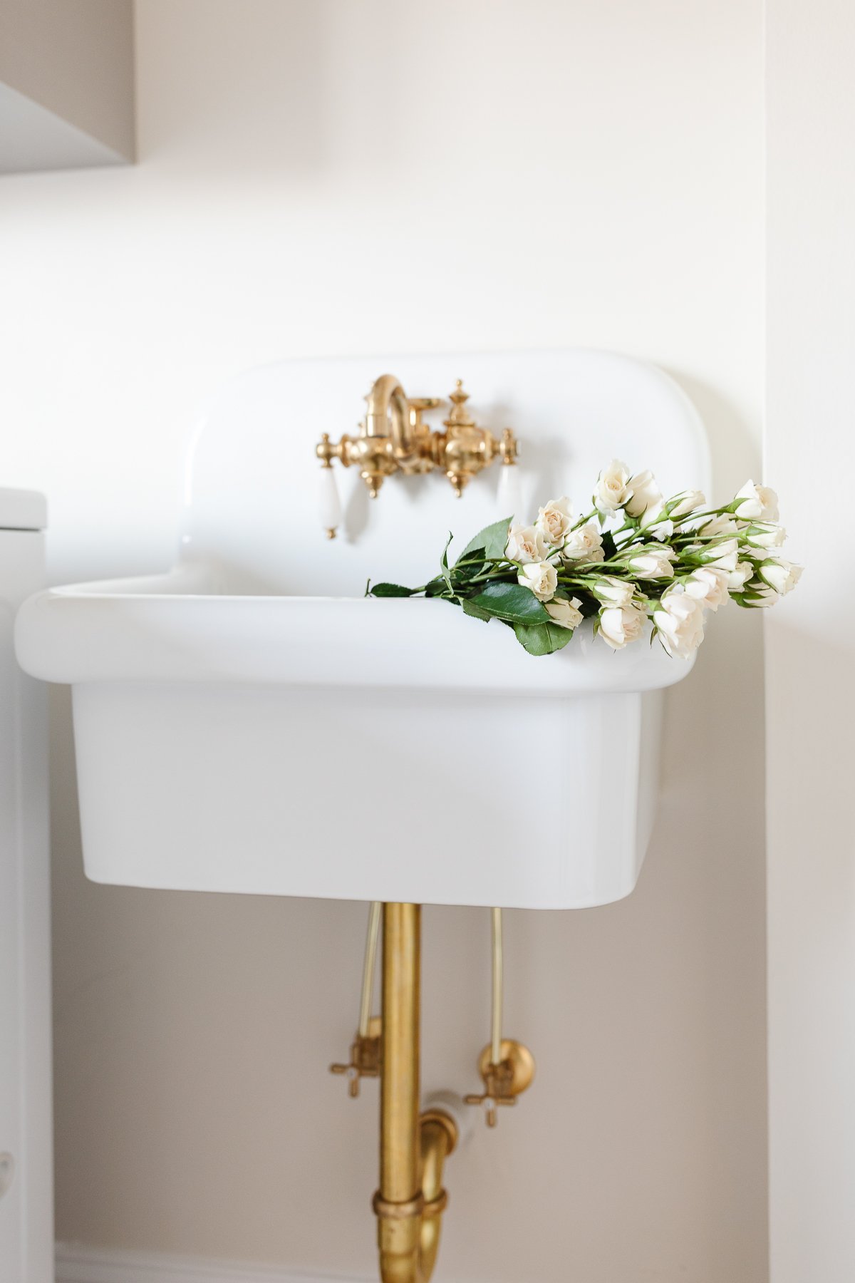A white sink with a gold faucet in a second level laundry room, adorned with beautiful flowers.