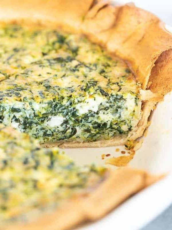 A spinach and feta quiche in a white pie pan, one slice removed.