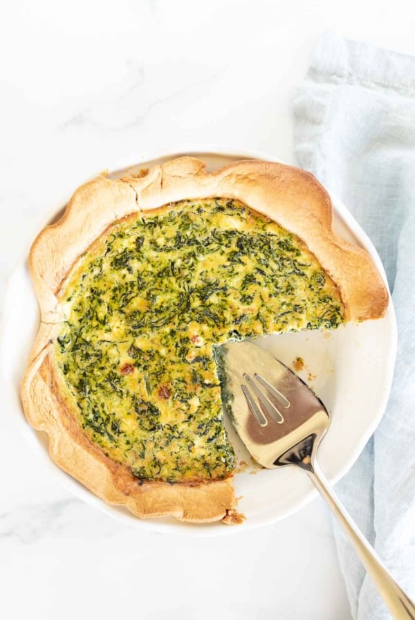 A freshly baked spinach and feta quiche with a slice being served.