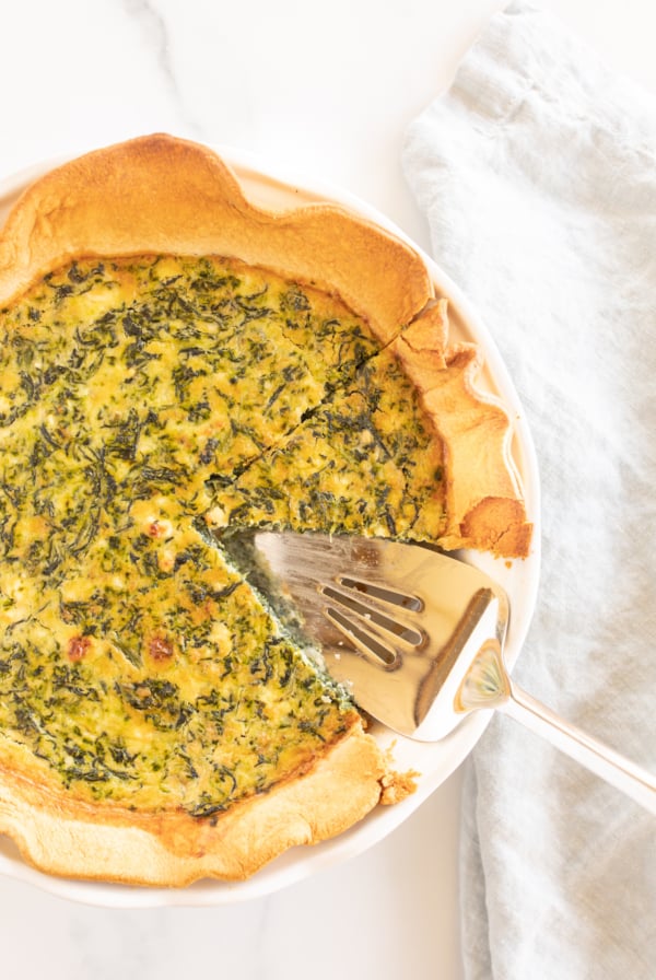 Spinach and feta quiche in a white pie pan with slice removed.