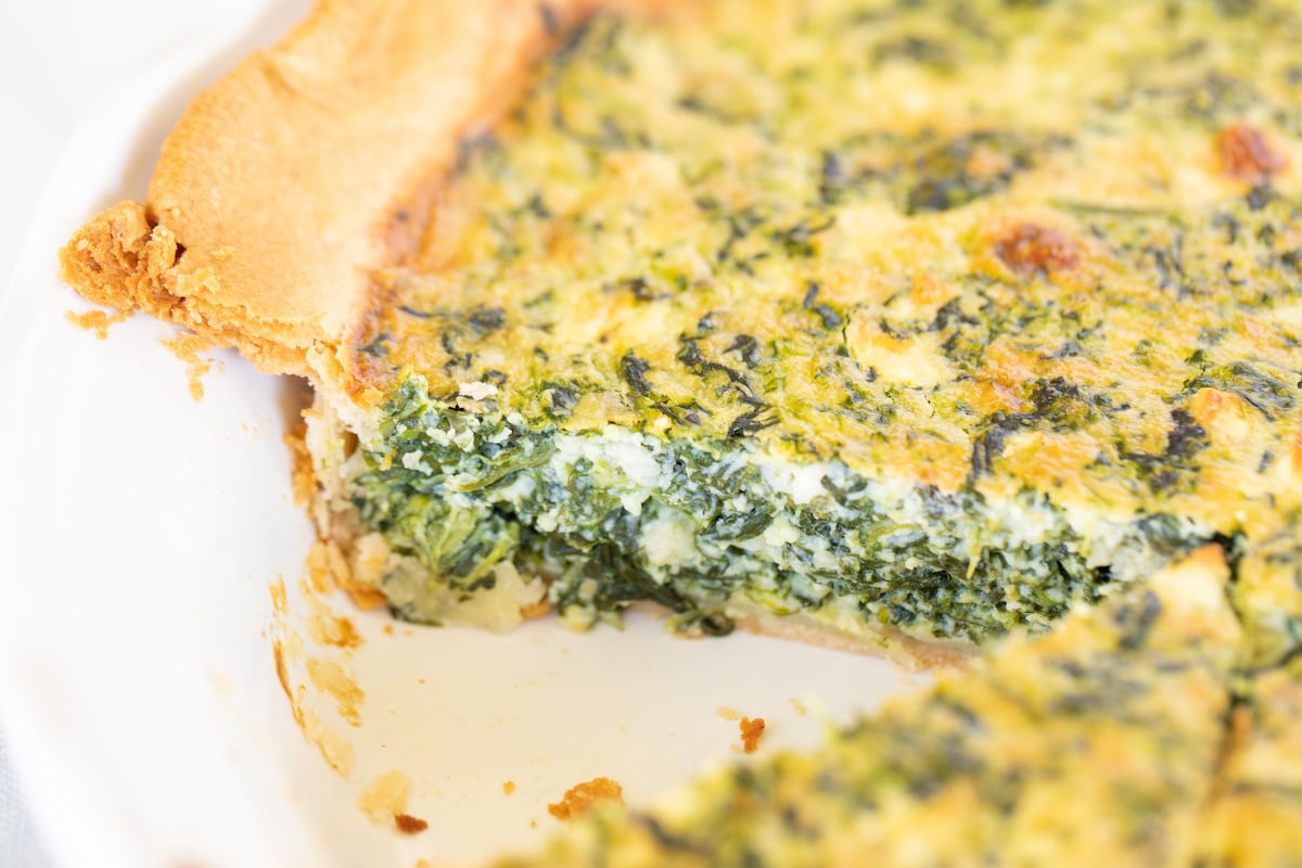 Spinach and feta quiche in a white pie pan with slice removed.
