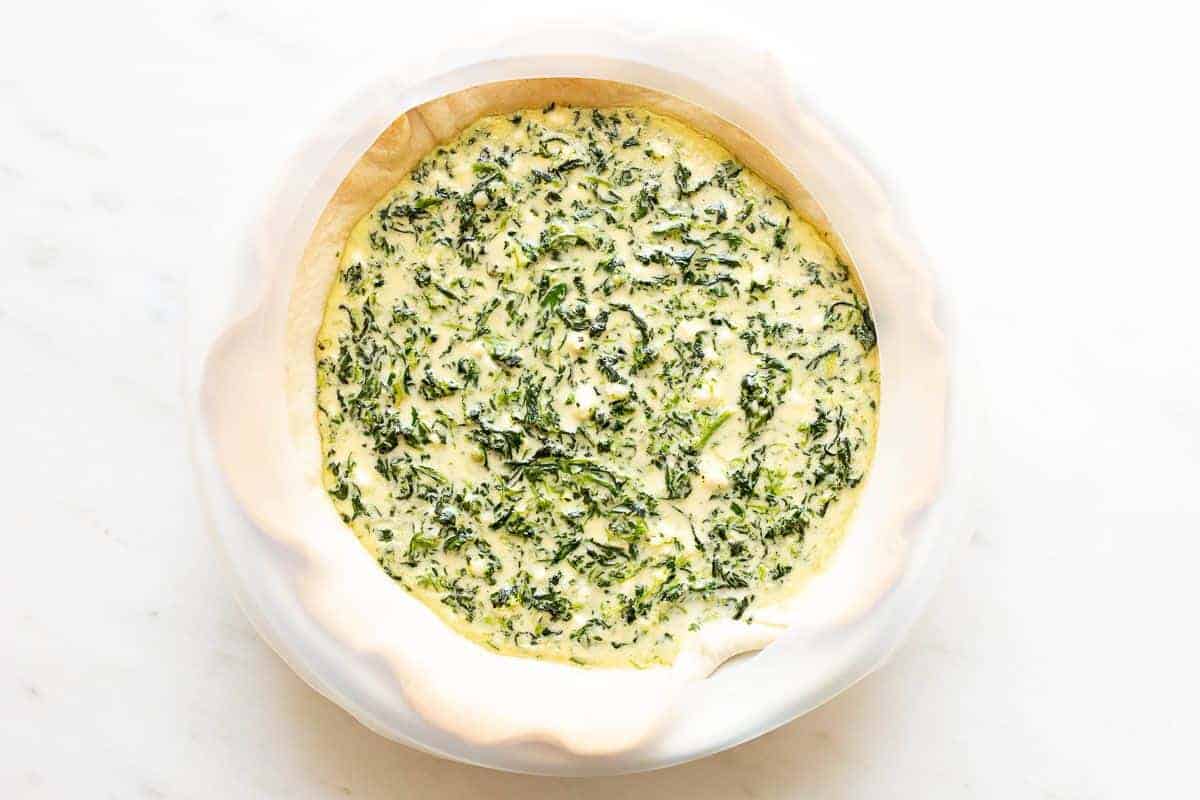 A small unbaked spinach quiche on a marble surface.