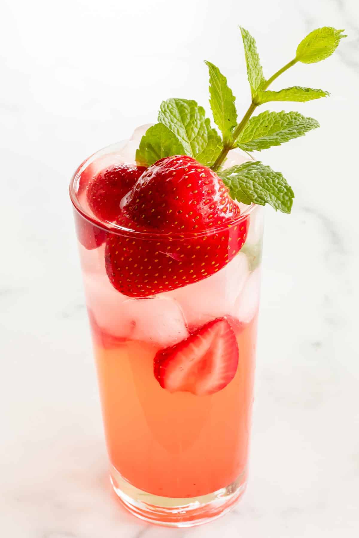 strawberry mojito in clear cocktail glass garnished with mint and lime wedges