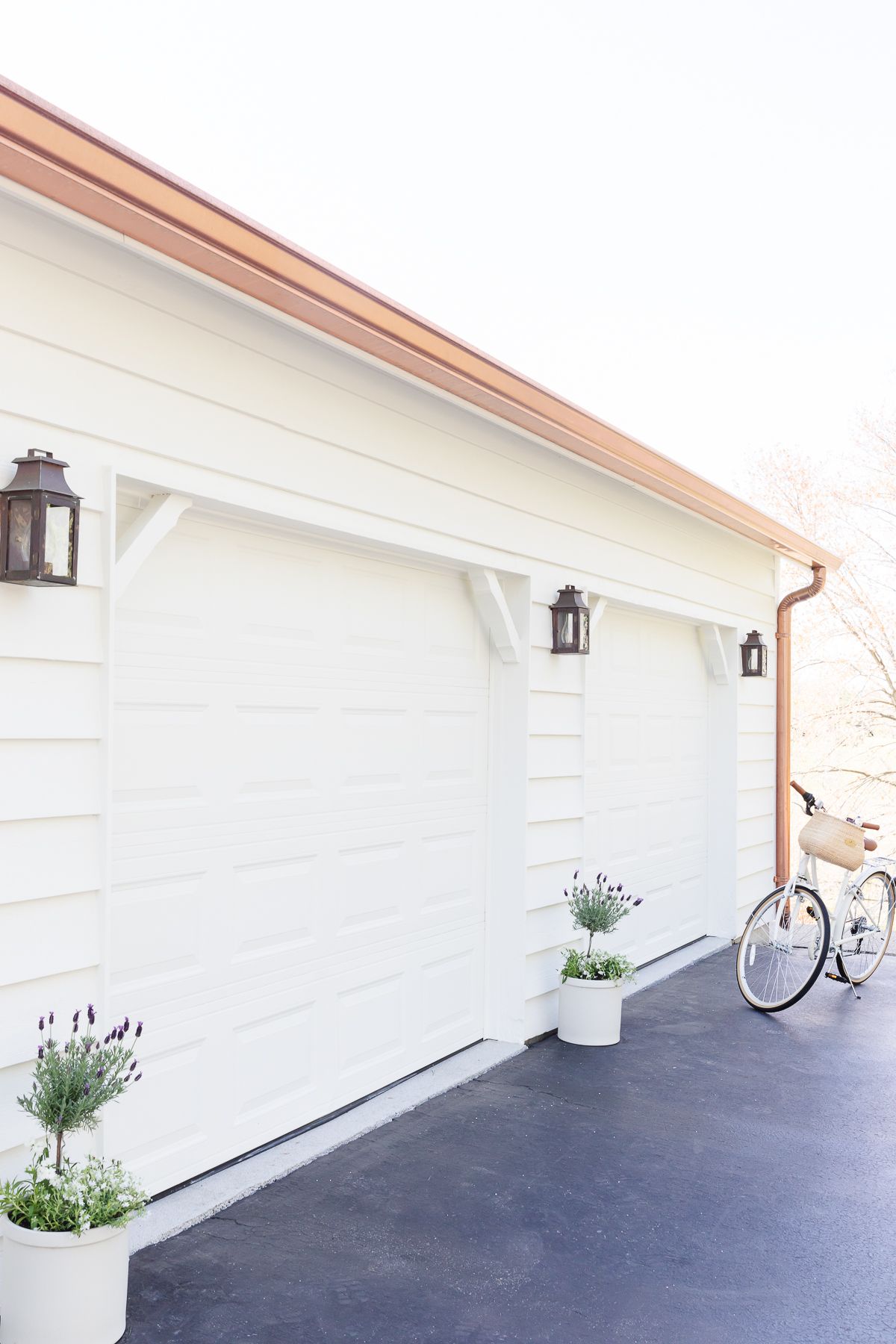 Garage doors of a home, painted in a soft cream color, with copper gutters and copper lanterns.