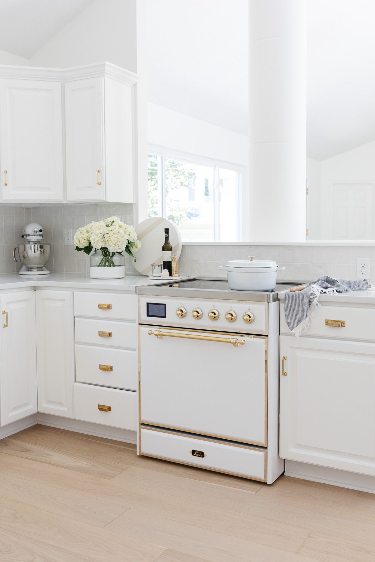 A white kitchen with a white and brass ILVE range, with white oak flooring