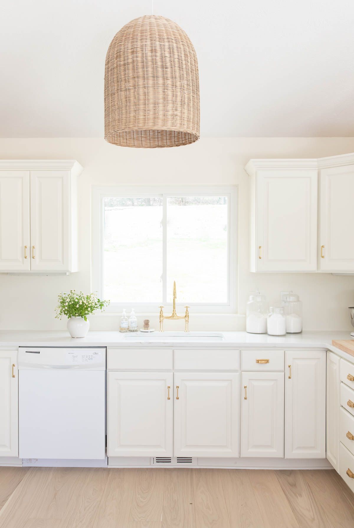 A white kitchen with white oak floors and a woven pendant