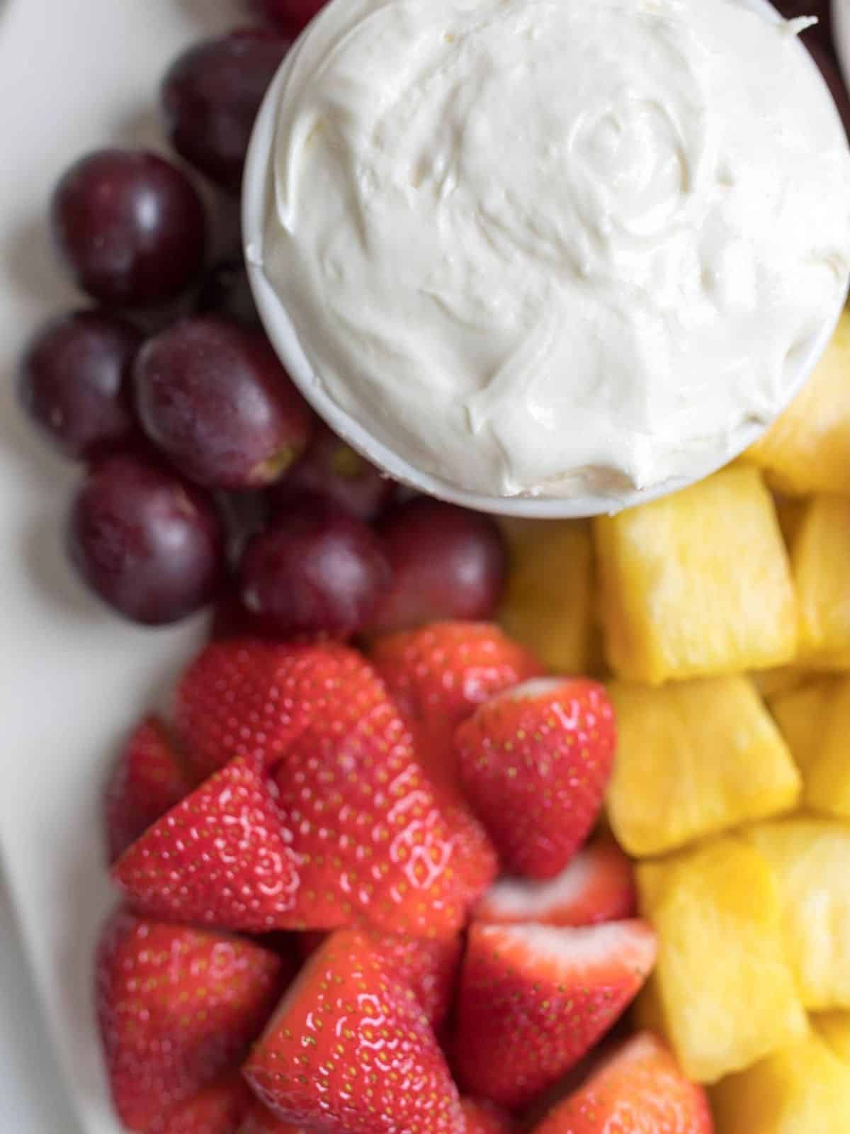 white tray holding cream cheese dip and fresh fruits.