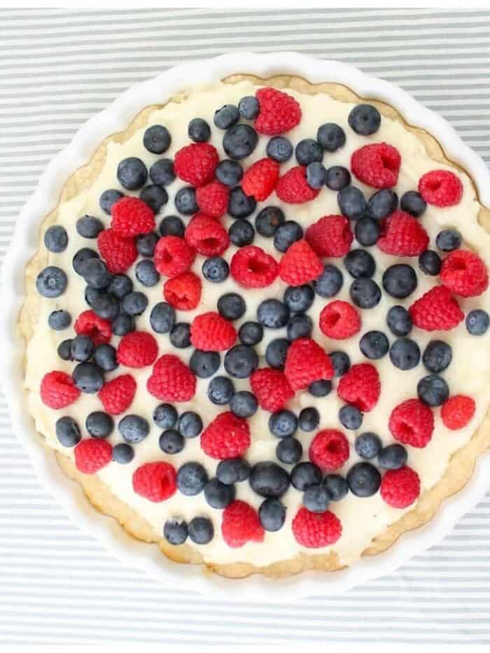 On a blue and white striped towel is a tart topped with berries in a white pie dish.