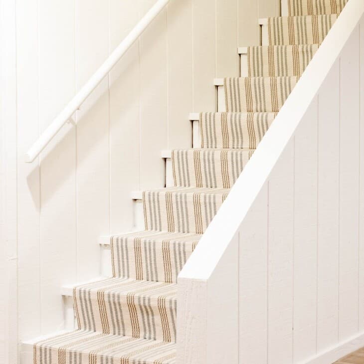 Basement stairs with a striped runner and Benjamin Moore Swiss Coffee warm cream paint color on the walls.