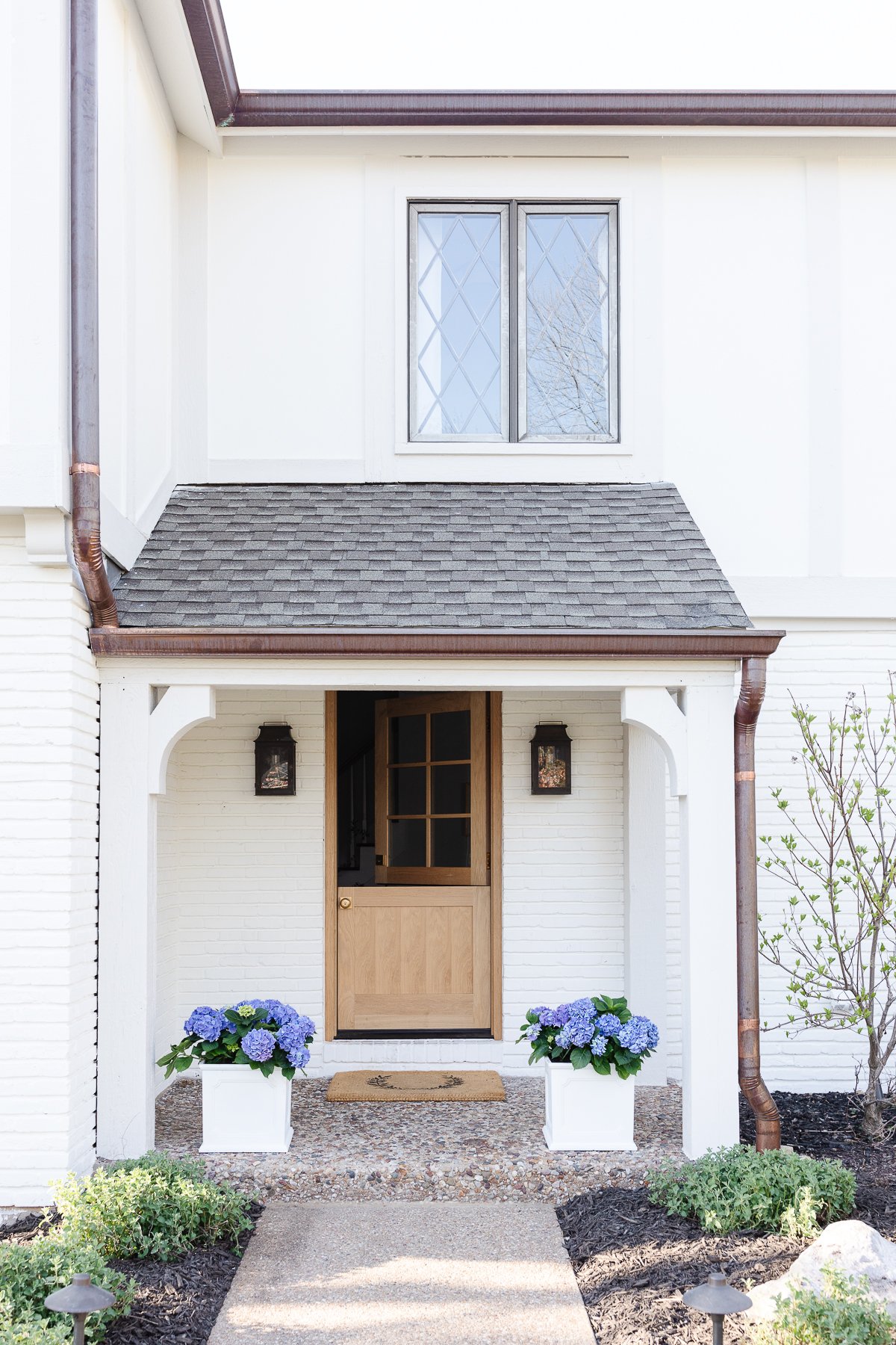 A front entrance of a house with a Benjamin Moore Swiss Coffee exterior, wooden door, and two potted plants.