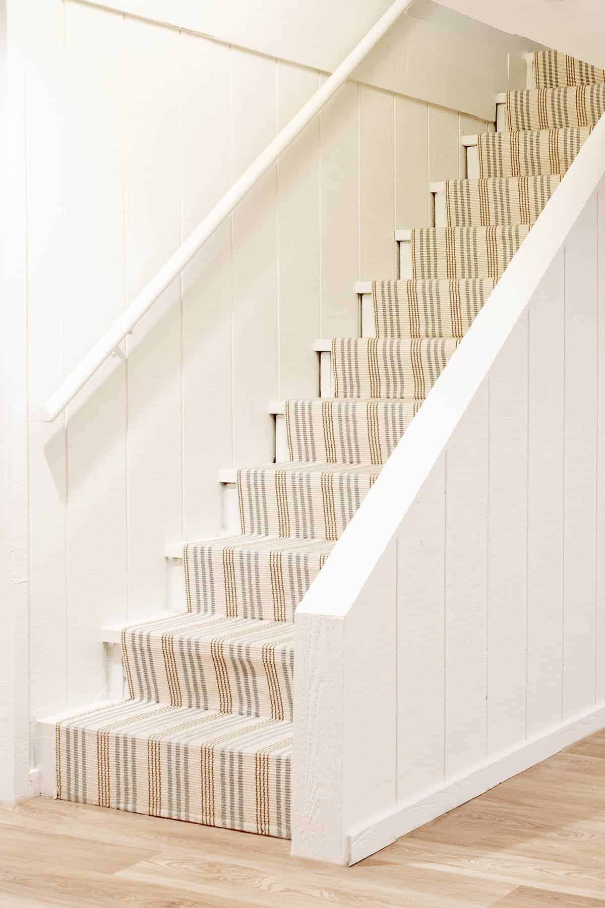 Basement stairs with a striped runner and Benjamin Moore Swiss Coffee warm cream paint color on the walls.