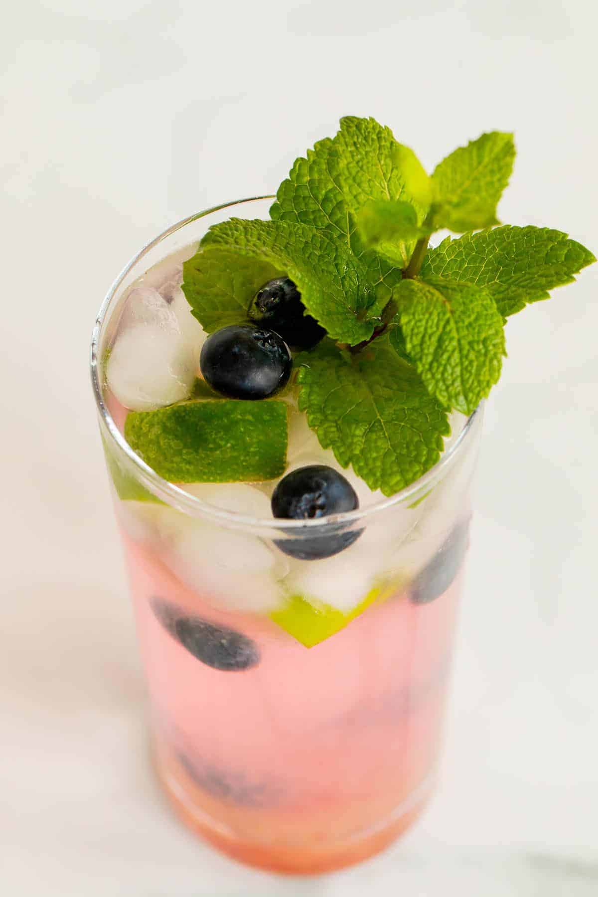 A fresh blueberry mojito garnished with mint, lime and blueberries on a marble surface.