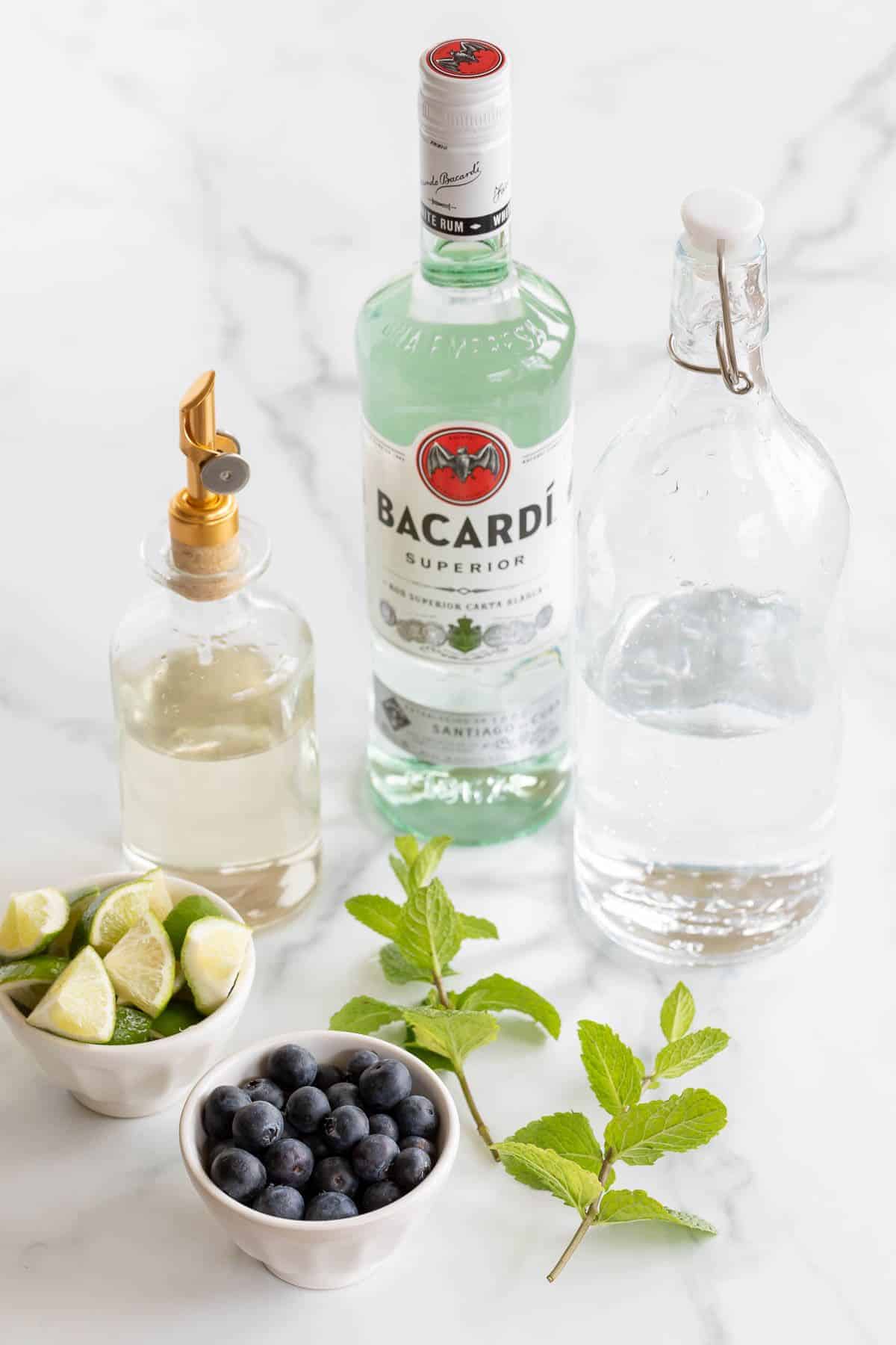 Ingredients for a blueberry mojito cocktail on a marble surface.